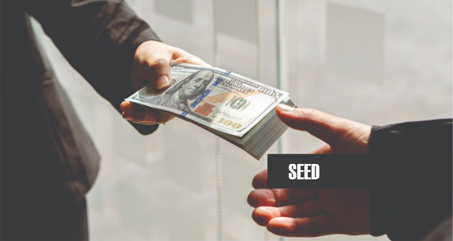 Hands exchanging a stack of U.S. dollar bills labeled SEED